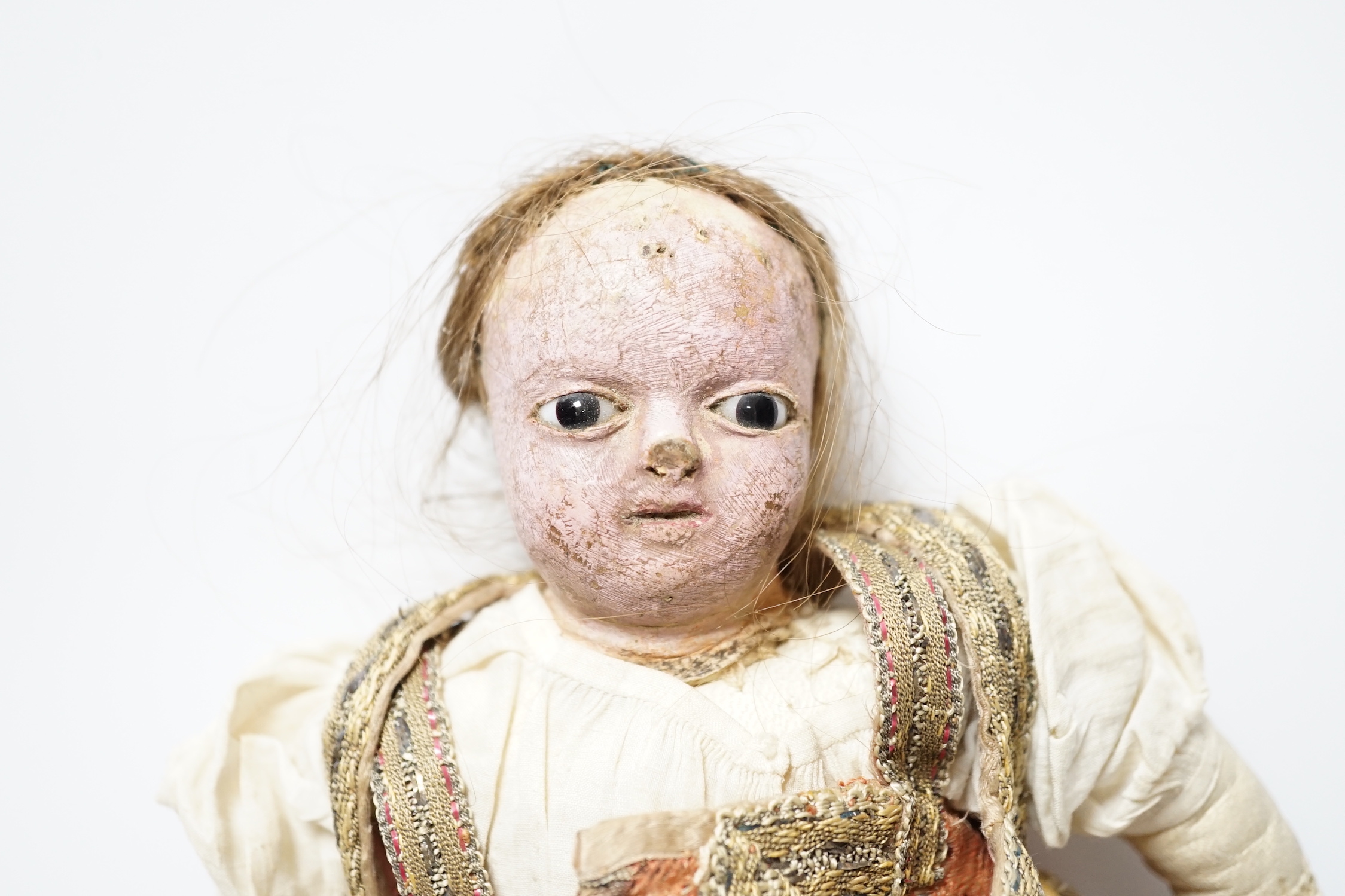 An early 19th century doll with a papier mache head, glass eyes and kid leather body, dressed in 18th century embroidered brocade and silk costume, possibly religious, 40cm high